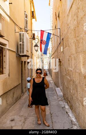 PAG, CROAZIA - 13 luglio 2021: Un'immagine verticale di una donna posingon una strada stretta con negozi nella città di Pag, Croazia Foto Stock