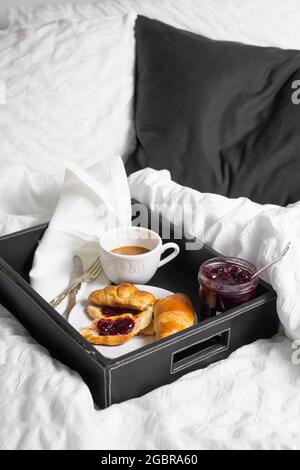 Colazione con croissant e tazza di caffè servita in un vassoio a letto con biancheria bianca. Foto Stock