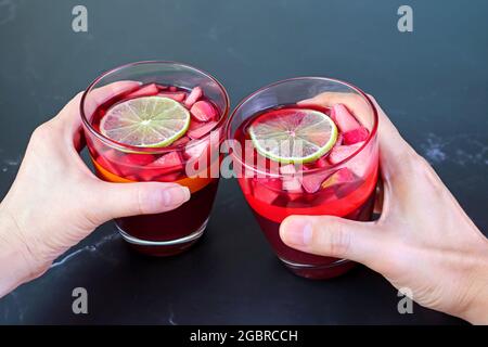 Donna e mano dell'uomo che tiene il bicchiere di vino rosso Sangria sul tavolo nero Foto Stock