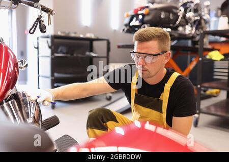 Uomo riparatore in occhiali di protezione raccogliendo vernice per moto in officina di riparazione auto Foto Stock