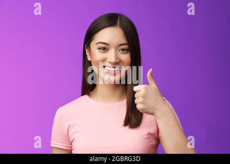 Amichevole buon-sguardo che sostiene l'amica asiatica della femmina lo incoraggia a continuare andare, lavoro piacevole, buon lavoro soddisfatto, approvazione sorridente, mostra il gesto del pollice-in su Foto Stock