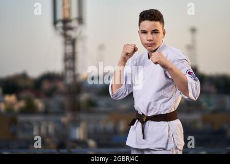 Giovane ragazzo praticante di karate in bianco kimono allenamento sul tetto al tramonto Foto Stock