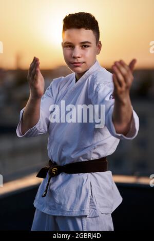 Giovane ragazzo praticante di karate in bianco kimono allenamento sul tetto al tramonto Foto Stock