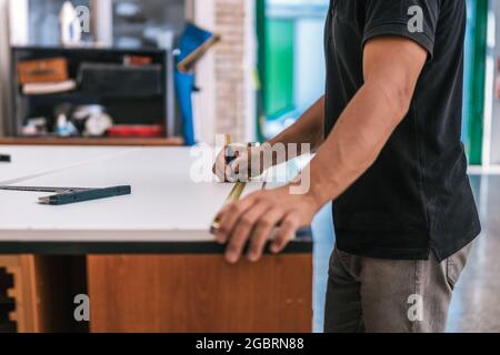 Mano di un uomo che usa una matita per contrassegnare un punto misurato su una superficie in un'officina Foto Stock