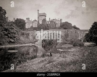 Una vista del tardo 19 ° secolo di un pescatore presso il fiume Blackwater a Lismore, County Waterford, Irlanda. Dietro si trova il ponte Cavendish, noto anche come ponte Lismore costruito nel 1858. Sovrasta entrambi il castello di Lismore, sede del duca del Devonshire. Fu in gran parte ricostruita per William George Spencer Cavendish, VI Duca del Devonshire, in stile gotico dall'architetto William Atkinson dal 1812 al 1822. Nel 1850 il 6° duca ingaggiò il suo architetto Sir Joseph Paxton, il progettista del Palazzo di Cristallo, per apportare miglioramenti e aggiunte al castello. Foto Stock