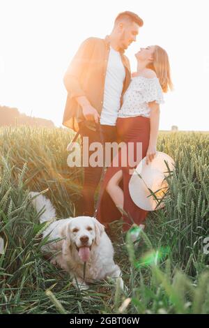 Nei raggi del sole della sera, tutti sono felici: Giovane coppia incinta e il loro grande cane bianco. Donna incinta . Famiglia e gravidanza. Amore e tendenza Foto Stock