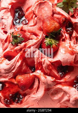 Gelato al gusto di fragola congelato - dettaglio a cornice. Primo piano di una superficie rosa di gelato coperto con pezzi di frutta rossa. Foto Stock