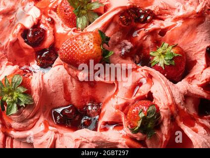 Gelato al gusto di fragola congelato - dettaglio a cornice. Primo piano di una superficie rosa di gelato coperto con pezzi di frutta rossa. Foto Stock