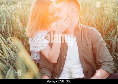 Bella giovane coppia irradia una tenerezza sconfinata l'una per l'altra seduta in campo tra erba alta . Amore e tenerezza. Bei momenti di vita Foto Stock