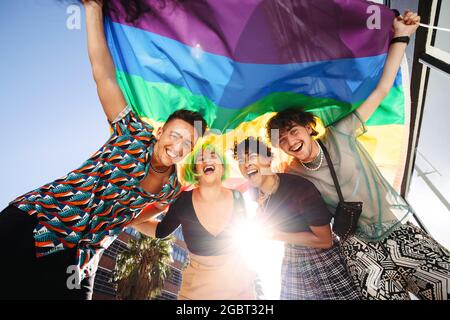 Giovani allegri che celebrano le loro identità in una sfilata di orgoglio gay. Gruppo di giovani LGBTQ sorridono allegro mentre alzano l'arcobaleno Foto Stock