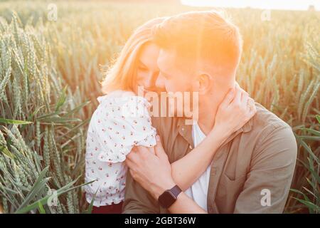 Felice giovane coppia abbraccia, seduta in erba alta in campo in raggi di sole di estate. Amore e tenerezza. Bei momenti di vita. Gioventù e b Foto Stock