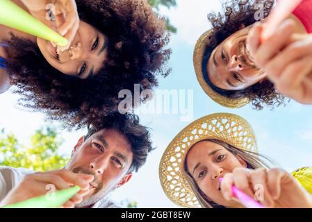 sotto la vista di quattro amici felici che tengono cannucce bere da un cocktail estivo all'aperto durante l'happy hour. divertente basso pov ritratto tagliato di persone Foto Stock