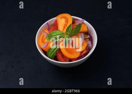 Insalata di pomodoro fresca con cipolla e basilico su fondo scuro. Miscela di pomodori rossi e gialli Foto Stock