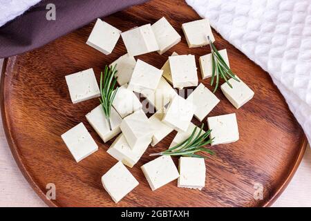 Vista dall'alto dei cubetti di tofu vegetariani con rosmarino fresco su sfondo di legno. Foto Stock