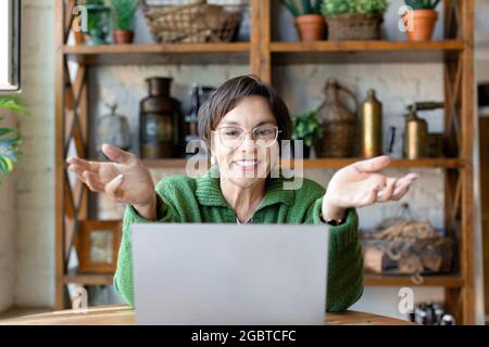 Ritratto in primo piano di una donna anziana davanti al monitor del computer portatile durante la videochiamata online. Lei sorride e gestura a mani. Foto Stock
