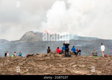 Persone che whatching l'eruzione del vulcano Fagradalsfjall dalla cima di una collina in Islanda in una giornata estiva parzialmente nuvolosa Foto Stock