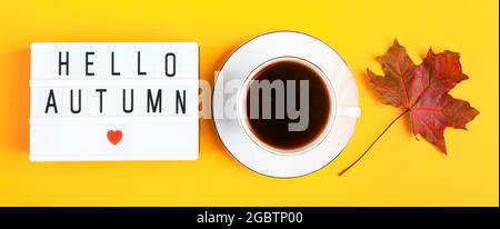 Ciao autunno concetto. Tazza di caffè e un segno con iscrizione su sfondo giallo. Foglie cadute e bevanda calda. Formato banner Foto Stock