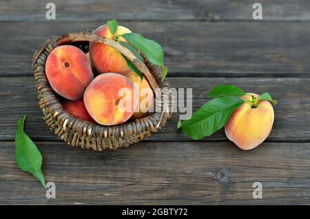 Cesto di vimini con frutta di pesca matura e succosa su un rustico tavolo di legno. Concetto di crescita del proprio cibo organico. Foto Stock