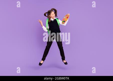 Foto di positivo pittore schoolgirl salto tenere pallet sguardo lato usura zaino uniforme isolato viola colore sfondo Foto Stock