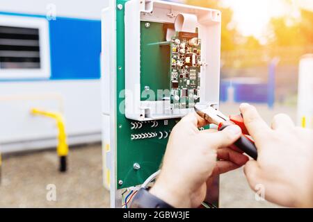 Regolazione dell'apparecchiatura di controllo e misurazione. Le mani di un elettricista o di un ingegnere con pinze al lavoro da vicino. L'appaltatore esegue i lavori nello stabilimento di produzione. Foto Stock