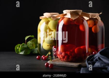 Tre barattoli fatti in casa di frutta in scatola in grandi vasetti di vetro su tavola nera. Spazio per il testo. Foto Stock
