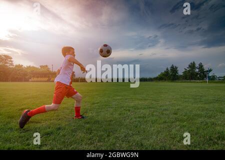 Ragazzo che gioca con la palla di calcio sul campo da gioco. Divisa da calcio bianca - rossa. Foto Stock