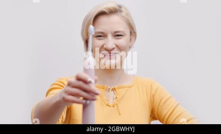 Ragazza carina che tiene uno spazzolino elettrico a ultrasuoni. Ragazza vestita con un top giallo. Routine mattutina. Cura dentale. Concetto di igiene personale. Isolato girato su sfondo bianco studio. Foto Stock
