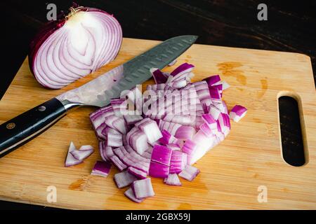 Cipolla rossa tagliata su un tagliere di bambù: Cipolla rossa tagliata e un coltello da cucina su un tagliere di legno Foto Stock