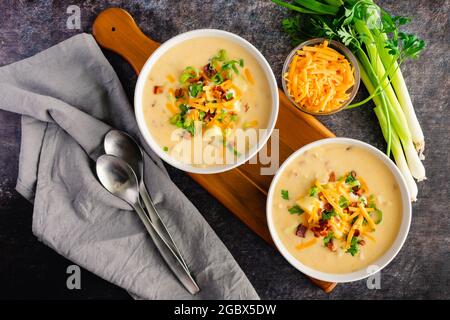 Ciotole di zuppa di patate al forno con panna acida, formaggio Cheddar, pancetta e cavoli: Zuppa di patate cremosa guarnita con panna acida, ch tritato Foto Stock