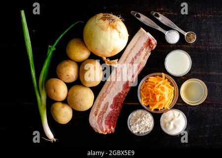 Ingredienti di zuppa di patate al forno caricati su un tavolo di legno: Patate crude, formaggio grattugiato, pancetta, panna acida e altri ingredienti Foto Stock