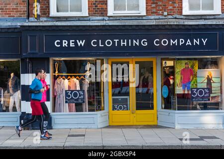 Inghilterra, Hampshire, Petersfield, coppia che fa jogging passato Crew Clothing Company Shop Front Foto Stock