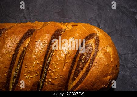 Insolita pagnotta di pane fresco a due colori su sfondo nero, foto in un tasto basso in luce dura, primo piano. Foto Stock