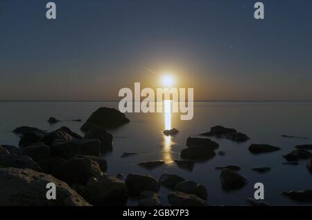 Luna piena sul mare di notte con un riflesso in acqua Foto Stock