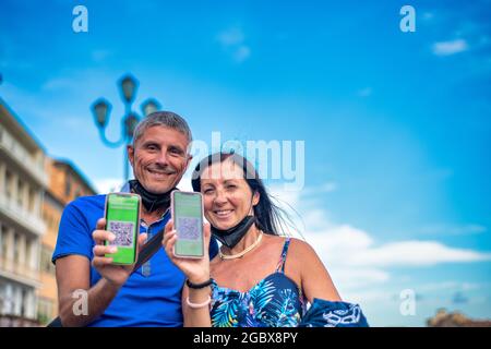 Felice coppia che visita la città con il covid green pass. Uomo e donna pronti a fare un viaggio con screenshot della vaccinazione Foto Stock