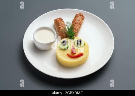 faccia sorridente del coniglietto da patate schiacciate e tagli di carne per i bambini su piatto bianco Foto Stock