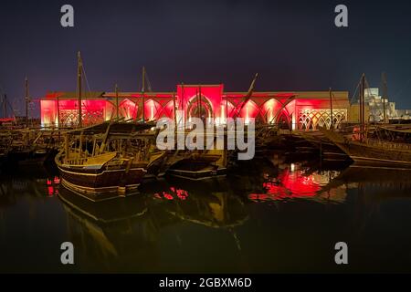 Le tradizionali barche in legno chiamate Dhows di fronte alla sala illuminata al Sukyum di Doha di notte, Qatar, Medio Oriente di fronte al cielo scuro e limpido Foto Stock