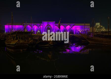 Le tradizionali barche in legno chiamate Dhows di fronte alla sala illuminata al Sukyum di Doha di notte, Qatar, Medio Oriente di fronte al cielo scuro e limpido Foto Stock