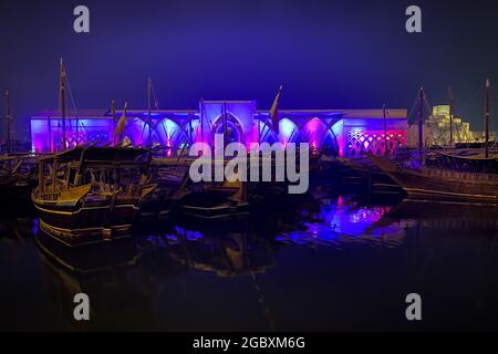 Le tradizionali barche in legno chiamate Dhows di fronte alla sala illuminata al Sukyum di Doha di notte, Qatar, Medio Oriente di fronte al cielo scuro e limpido Foto Stock