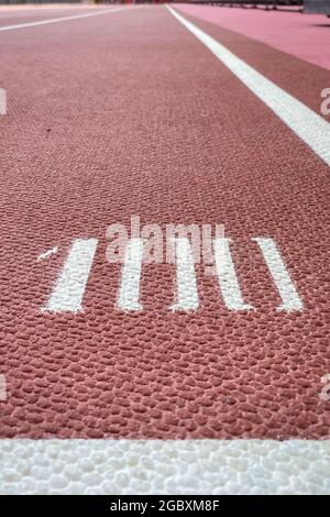 Il numero 100 su una corsia rossa su una pista atletica con linee bianche Foto Stock