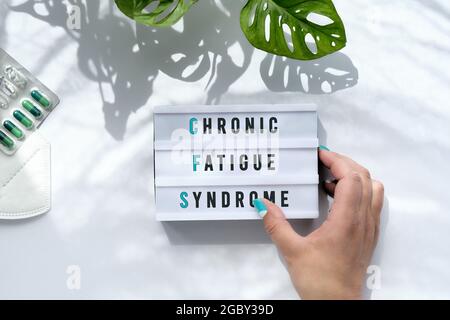 Texte sur Chronic Fatigue Syndrome or CFS on light box in hand. Progettazione di consapevolezza delle malattie a lungo termine. Sfondo bianco con foglie di monstera trendy e lungo Foto Stock