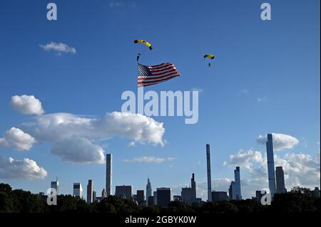 New York City, Stati Uniti. 05 agosto 2021. Lo skyline di Manhattan è visto dietro due membri della squadra di paracadute della marina degli Stati Uniti "Leap Frogs" mentre si vola una bandiera degli Stati Uniti durante il loro atterraggio sul Great Lawn in Central Park, New York, NY, 5 agosto 2021. La squadra di paracadute US Navy Leap Frog è iniziata nel 1969 e ha il compito di "dimostrare l'eccellenza della Marina in tutti gli Stati Uniti". (Anthony Behar/Sipa USA) Credit: Sipa USA/Alamy Live News Foto Stock