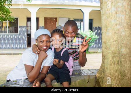 Madre africana e padre o tutore seduto insieme alla figlia in un ambiente scolastico, disponibile per aiutare la bambina a raggiungere l'eccellenza Foto Stock