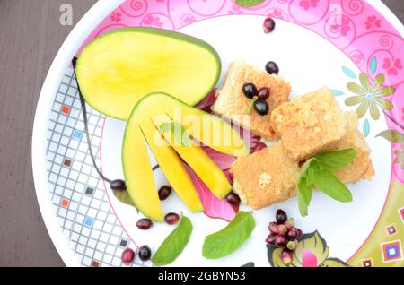 closeup il mango giallo verde affettato con torta di latte verde dolce j preambolo di frutta e foglie di menta su sfondo bianco marrone fuori fuoco. Foto Stock