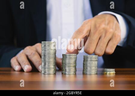 Contatto di uomo d'affari su pila di monete su tavola di legno, monete di impilamento dell'uomo per la pensione di soldi di risparmio, pila di monete degli uomini per l'investimento Foto Stock