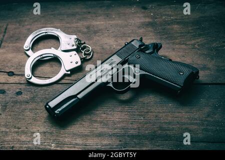 Pistola da 9 mm e manette su fondo in legno. Arma in metallo nero, pistola automatica su un tavolo vintage, concetto di giustizia del crimine. Vista laterale Foto Stock