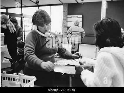 Austin, Texas USA, circa 1991: Impegnato addetto al check-out femminile presso il negozio di alimentari multi-task mentre aiutare il cliente. ©Bob Daemmrich Foto Stock