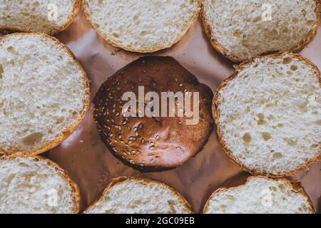 Pane Burger posto su un tagliere. Tagliere con fette di pane con semi di sesamo per preparare hamburger. Panini con sesamo per il mea macinato Foto Stock