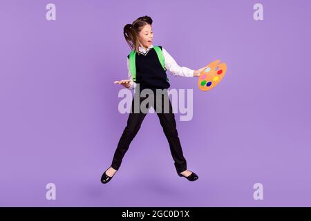 Foto di felice eccitato pittore scolargirl tenere pallet bocca aperta sacchetto di usura uniforme isolato viola di colore sfondo Foto Stock