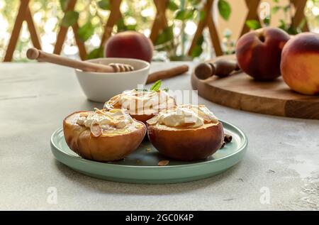 Pesche mature al forno con cannella, petali di mandorle, formaggio cremoso e miele in un giardino estivo. Messa a fuoco selettiva Foto Stock