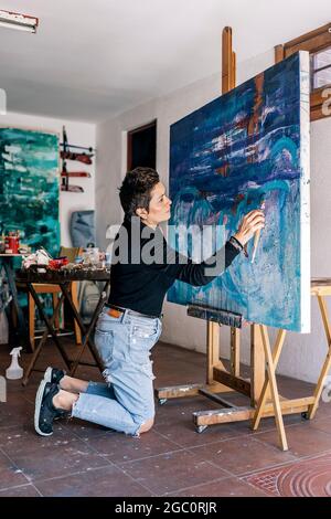 Pittore di mezza età messo a fuoco che lavora nel suo studio d'arte domestico ed usando la vernice blu. Foto Stock
